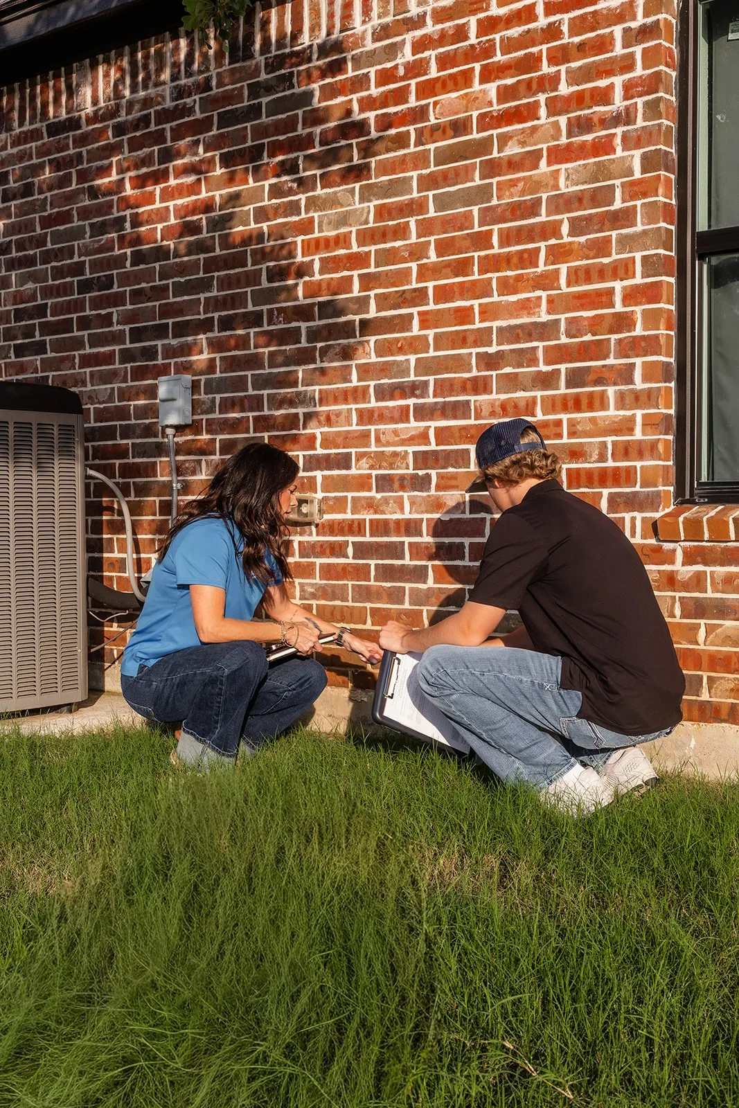 A-Custom team members examining a crack at the base of a brick wall
